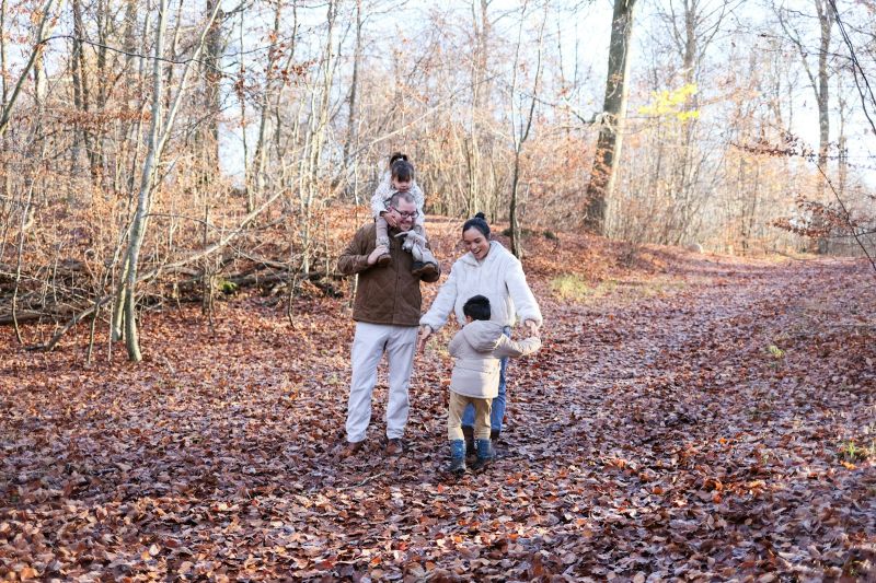 Familie mit zwei Kindern beim Spaziergang durch einen Wald voller Herbstlaub